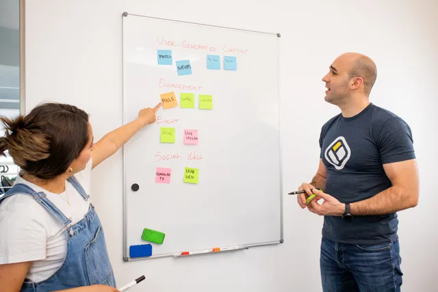 Two colleagues brainstorm on a whiteboard with colorful sticky notes for project planning. Customer Retention Plan Template for UK B2B Teams