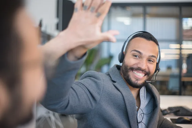 A cheerful call center agent with a headset gives a high five to a colleague in an office. Check these customer success software best tools for England