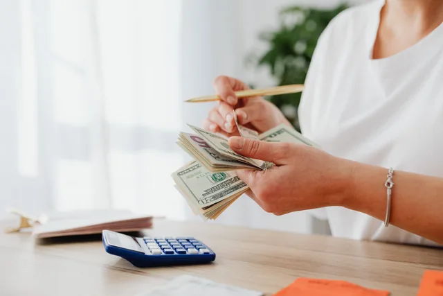 Close-up of a woman holding US dollars, calculating finances at home. Customer success software budget template: rows, owners and reviews