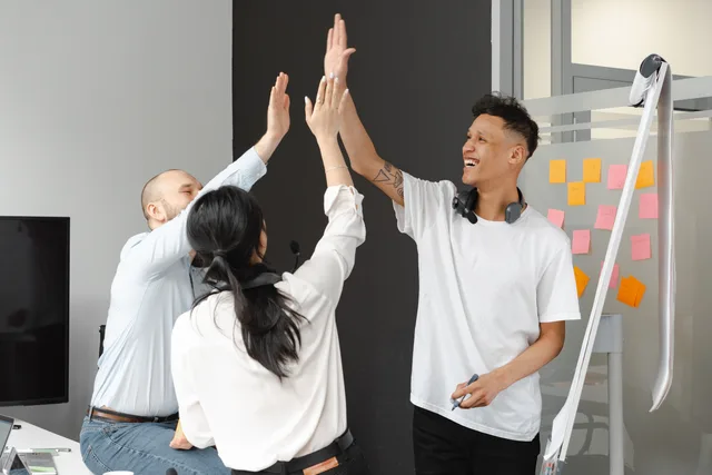 Diverse team members in an office high-fiving, symbolizing success and teamwork in a supportive environment. What are the customer success software business models?