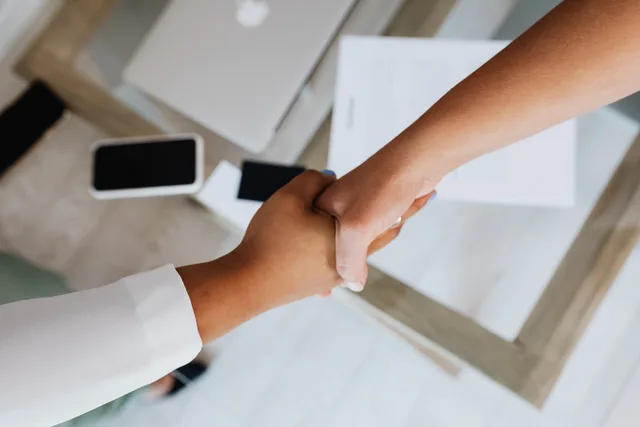 Two people shaking hands over a desk with modern tech, symbolizing a successful business agreement. What a customer success software commercial contract means for UK buyers