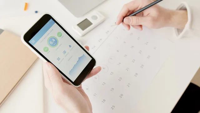 Close-up of hands using a smartphone to track health stats while planning on a calendar. How to score customer success software opportunities