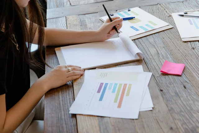 Businessperson in a workspace writing notes with charts and documents. Run customer success software competitor research as a checklist