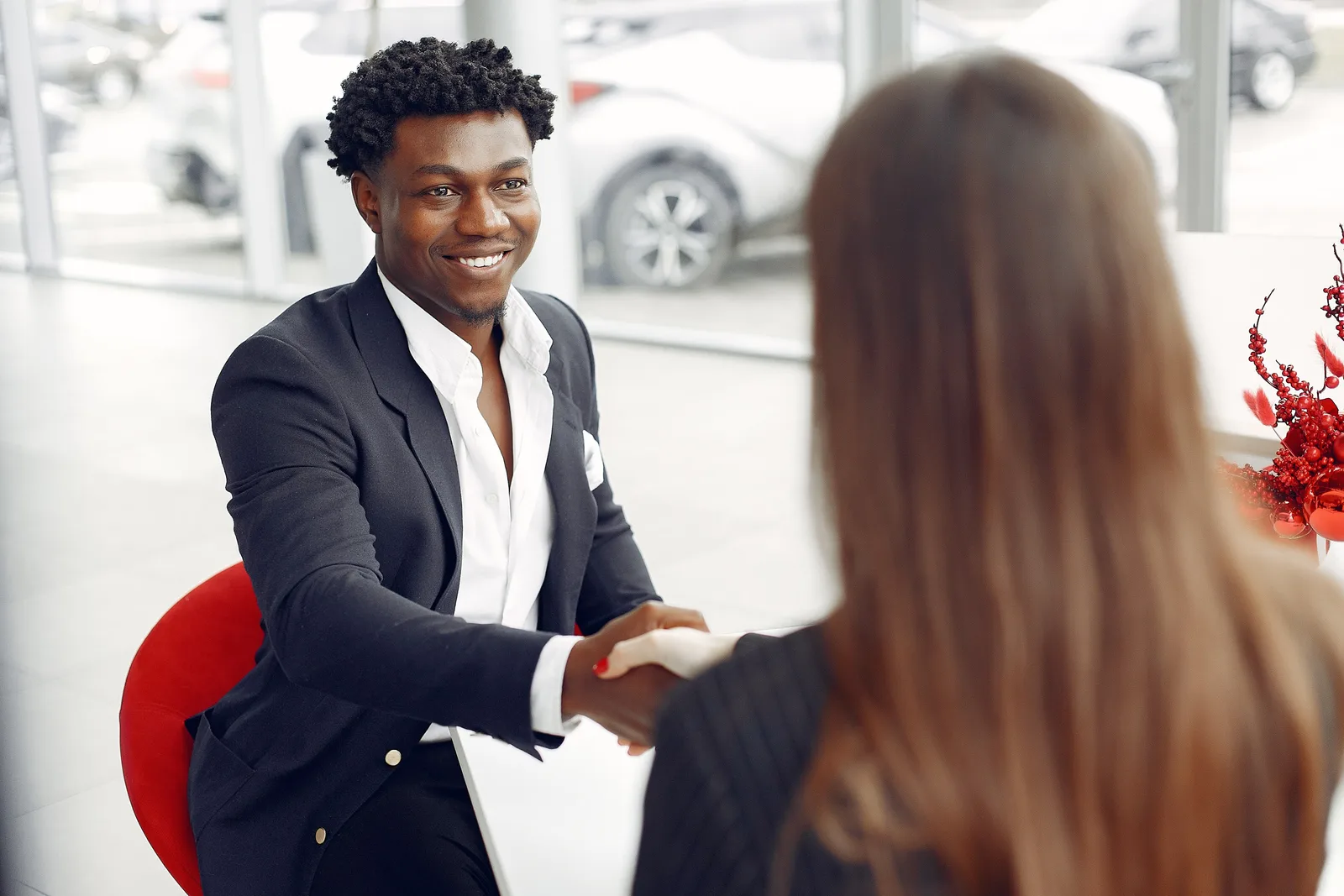 Cheerful happy African American customer in formal elegant suit shaking hands with female dealer after signing papers while smiling and looking at each other