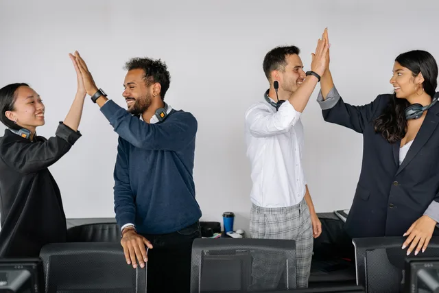 Diverse team of call center agents high-fiving in an office environment showcasing teamwork and collaboration. Seven customer success software hidden costs to price before you sign