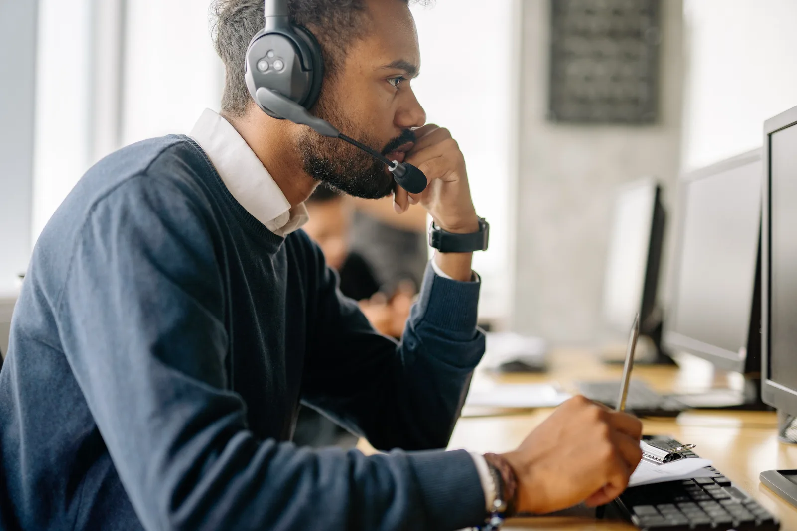 Side view of a bearded man in a headset concentrating at his desk in an office environment.