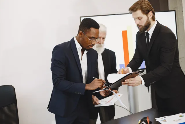 Three businessmen engaged in document signing in a modern office setting. Why customer success software return on investment needs a payback model
